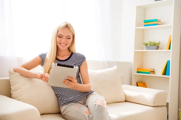 Happy woman sitting on couch and reading news on tablet