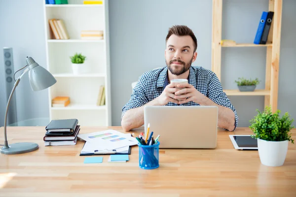 Young bearded man having break, drinking tea and dreaming