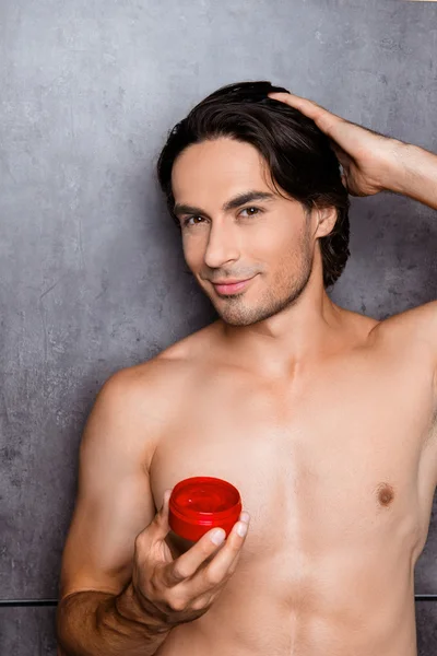 Muscular man holding jar of gel for hair and making hairstyle