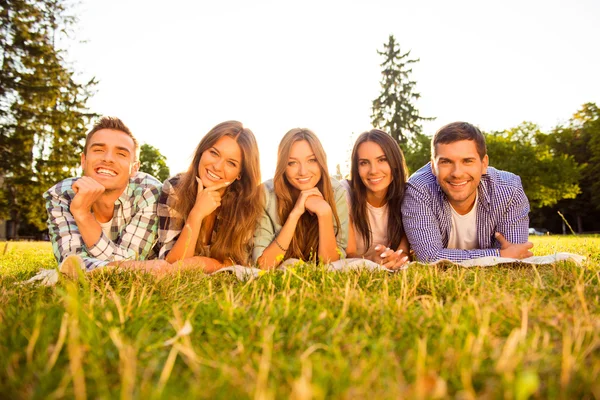 Five happy joyful boyfriends and girlfriends lying on grass and