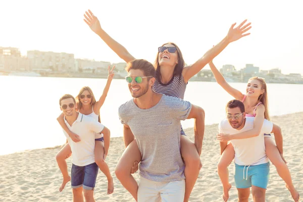 Outdoors photo of happy boyfriends piggybacking their girlfriend