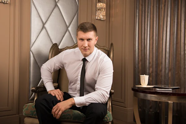 Thoughtful businessman in chic interior. thoughtful young man in a business suit sitting on the armchair with his legs crossed and keeps his hand on his chin