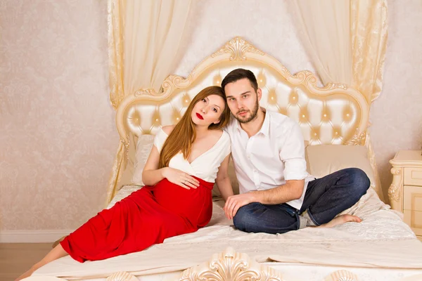 Young family expecting a baby. man and his pregnant woman sit on a big white bed