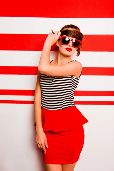 Cute girl with red lips and glasses posing against the striped b