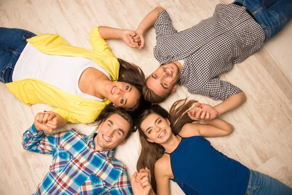 Cheerful young people lying on the floor holding hands
