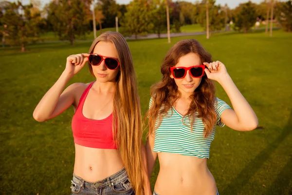 Two young slim girls holding hands and glasses in the park