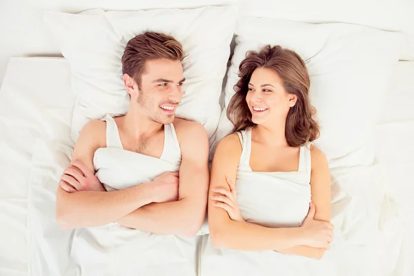 Beautiful funny couple in love lying in the bed crossing hands
