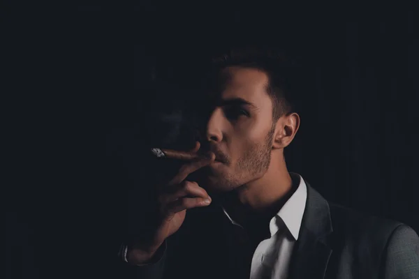 Handome confident man in suit on the black background smoking a