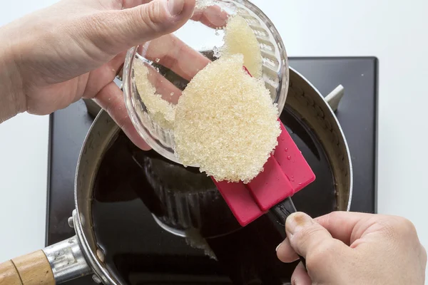 Pouring sugar into pan to cook sweet soup in the kitchen
