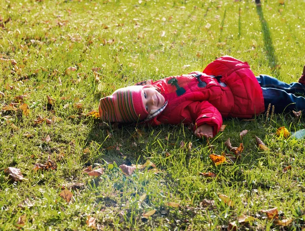 Little girl in a red jacket lying on the ground