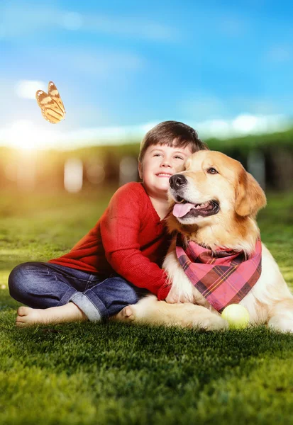 Little boy with a golden retriever dog sitting on the grass