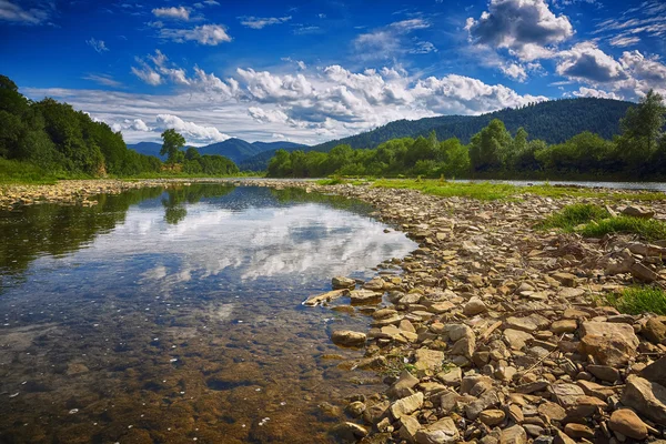 Clear river with rocks leads towards mountains