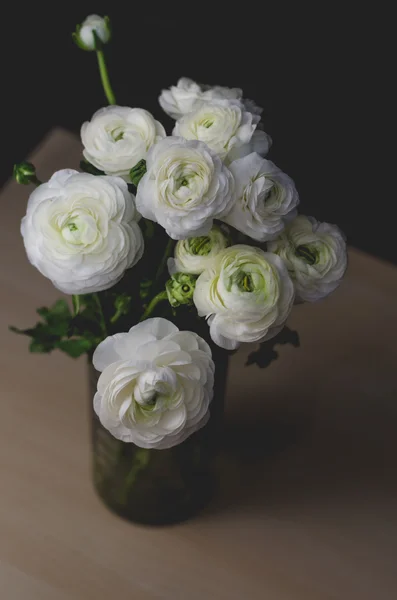 Bouquet white buttercup ranunculus bouquet of flowers in glass vase on a wood table. Still life, rustic style, dark tones.