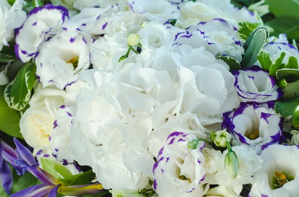 Rich white hydrangea, delicate cream roses, purple eustoma, lush leaves in a beautiful decoration. Big bouquet of fresh flowers on luxury wedding table. Summer background.