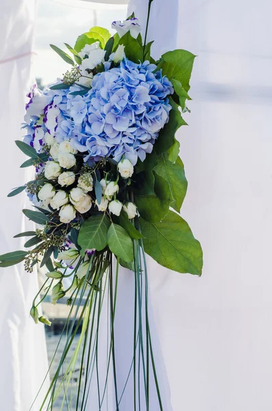 Flowers composition on luxury arch ceremony decorated with lush leaves, white hydrangea, delicate cream roses, purple eustoma, blue iris. Summer wedding concept sea theme. Floral arrangement.