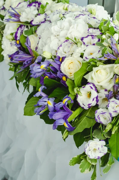 Luxury decoration with lush leaves, white hydrangea, delicate cream roses, purple eustoma, blue iris on a wedding table in banquet restaurant. Style summer sea marriage concept. Floral arrangement