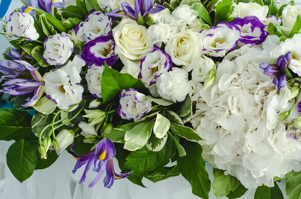 Luxury table beautiful, rich decoration with lush leaves, white hydrangea, delicate cream roses, purple eustoma, blue iris in restaurant. Style summer sea wedding concept. Floral arrangement.