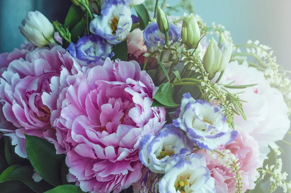 Rich bunch of pink peonies peony and lilac eustoma roses flowers, green leaf on blue background with sun light. Spring or summer lovely bouquet. Love concept. Card, text place, copy space.