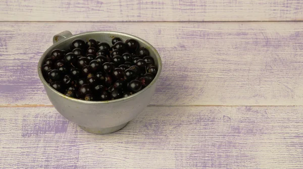 Black currant in white plate on  wooden retro background