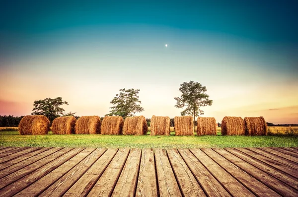Wooden planks floor with haystacks on the field in the background.