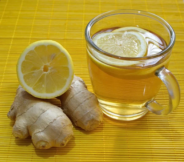 Glass of lemon tea with lemon pieces and ginger on the table