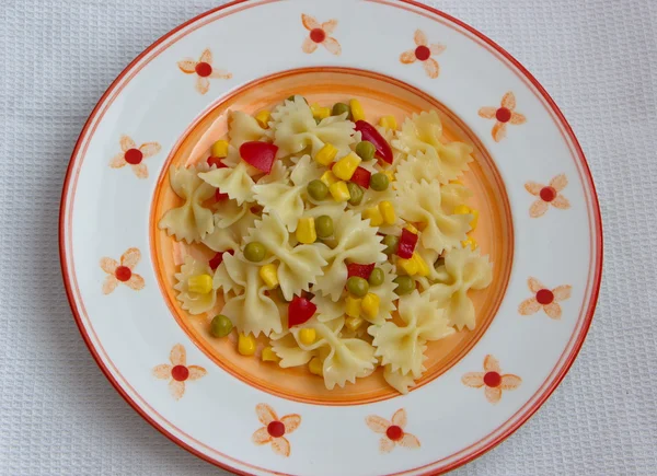 Farfalle with vegetables served on painted plate