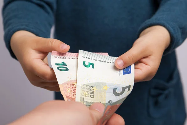 Small child hand takes five and ten euros banknotes from adult h