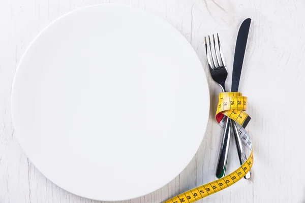 Plate, fork, knife and metering tape on wooden table