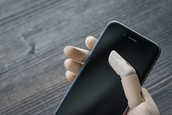 Artificial wooden hand with modern phone on wooden board