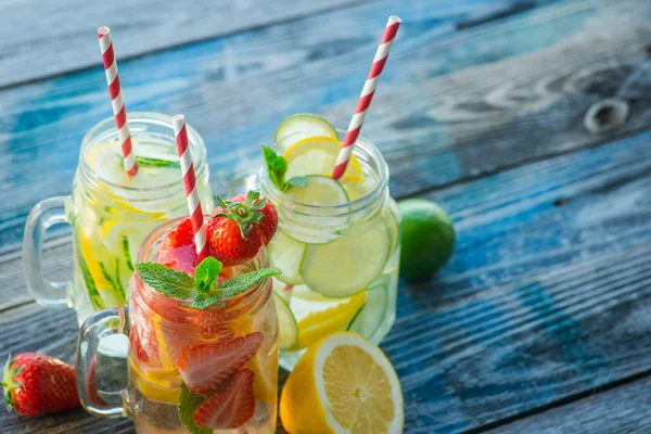 Jugs with lemon, lime, strawberry and cucumber infused water on a rustic wooden surface