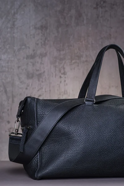 Black leather traveling bag, over the concrete wall background