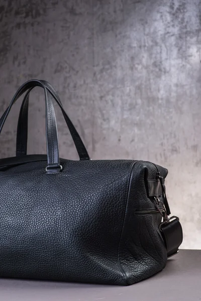 Black leather traveling bag, over the concrete wall background