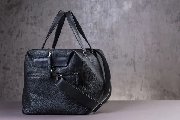 Black leather traveling bag, over the concrete wall background