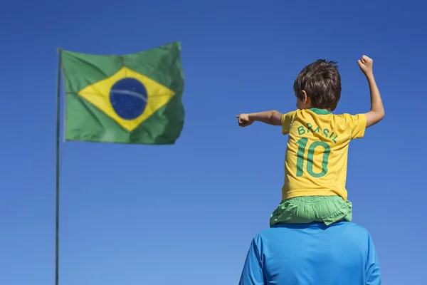 Boy and his father looking up at the Brazilian flag