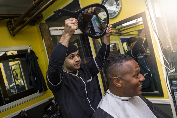 Barber shows haircut with mirror to client in a barber shop.