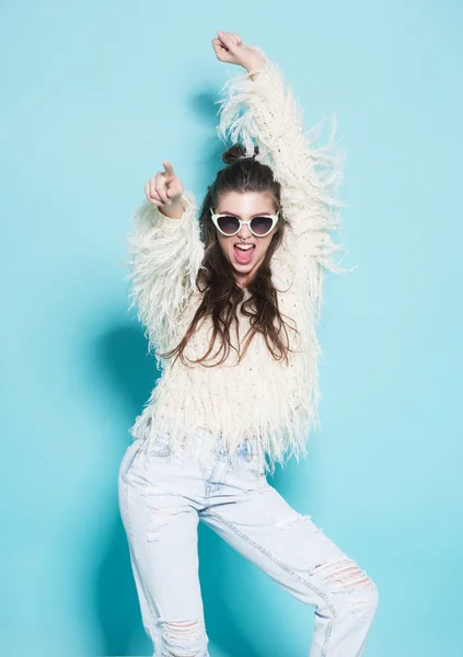 Portrait of cheerful fashion hipster girl going crazy making funny face and dancing. Blue color background.