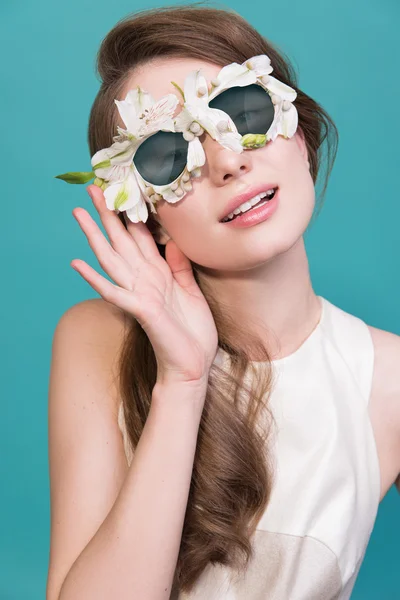Fashion portrait of beautiful young lady with flowers sunglasses on blue background