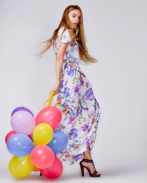 Fashion studio photo of beautiful model woman with blond hair in dress holding colorful balloons