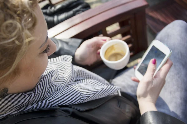 Young curly blond woman drinking coffee and  typing on the phone
