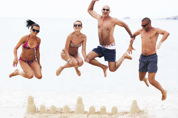 Four adults jumping on beach above sand castle