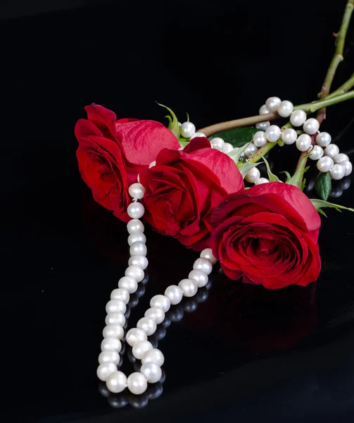 Red rose and pearls on black background