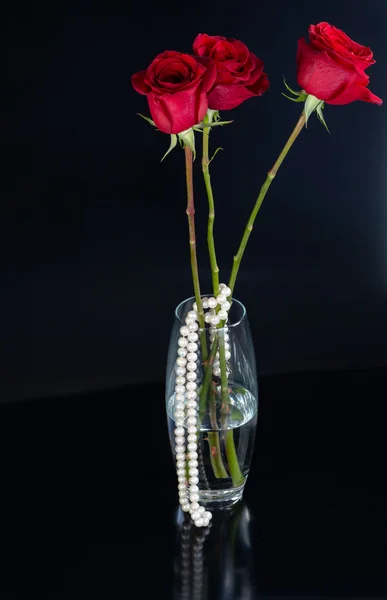 Red roses in a glass vase and necklace of white pearls