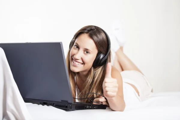 Girl with headphones listening to the music in a laptop on the bed