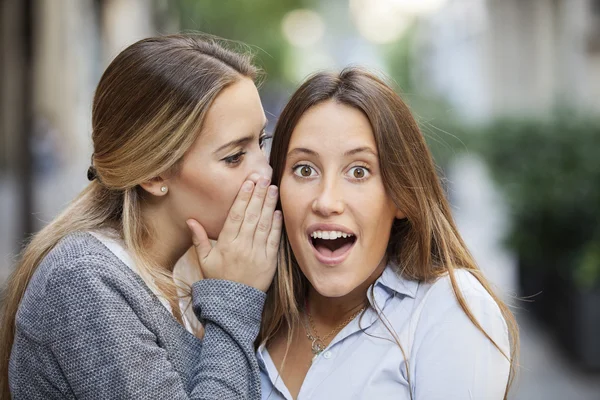 Attractive young woman whispering secret in friend's ear.