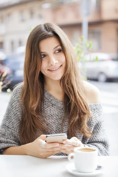 Beautiful girl sitting in a terrace bar and smiling while holding cell phone
