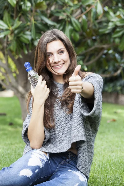 Smiling beautiful woman giving a thumbs up of approval for the bottle of fresh pure water that she is holding