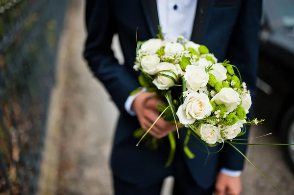 Groomsman hold in hand two bouquets for bridesmaids