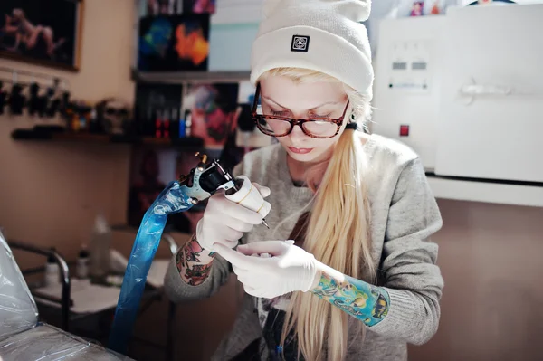 Portrait of a young blonde girl master tattooist in glasses and