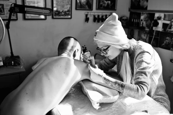 Young blonde woman master tattooist in glasses and hat with tatt