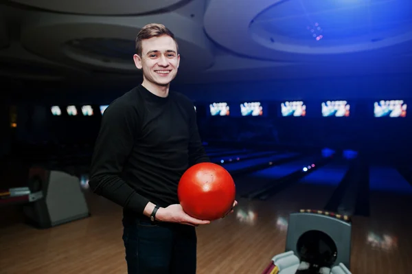 Cheerful young man holding a bowling ball and smiling at camera